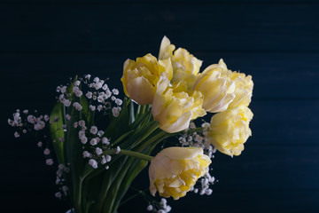Yellow tulips in a vase on a wooden background