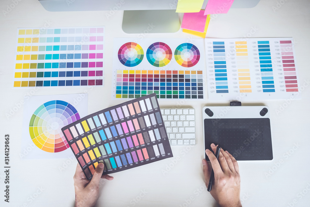Poster Image of male creative graphic designer working on color selection and drawing on graphics tablet at workplace with work tools and accessories, top view workspace