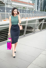 Young asian business woman holding gift bag and speaking to the phone outdoor