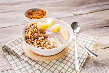 Obraz na płótnie Canvas Baked granola with nuts, cottage cheese, strawberry yogurt and pineapple slices in a plate on a checkered napkin. The light of the morning sun. Healthy breakfast