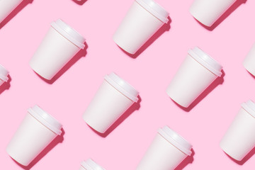 Pattern of disposable coffee cups on a pink background. Flat lay.