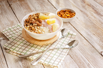 Baked granola with nuts, cottage cheese, strawberry yogurt and pineapple slices in a plate on a checkered napkin. The light of the morning sun. Healthy breakfast