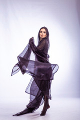 Naklejka premium beautiful young brunette girl in a black dress with a cape on a white background