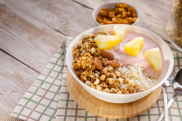 Close up baked granola with nuts, cottage cheese, strawberry yogurt and pineapple slices in a plate on a checkered napkin. The light of the morning sun. Healthy breakfast