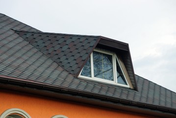 part of the roof of a private house under a tiled roof with a window against the sky