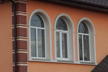 three large white windows on the brown concrete wall of a private house on the street