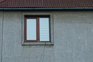 one brown large window on the gray plastered wall of a private house under a slate roof on the street