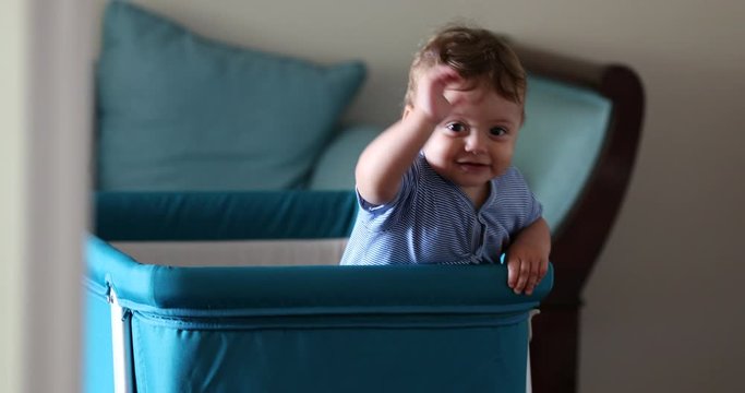 Baby inside crib wanting attention. Happy smiling toddler boy standing inside craddle