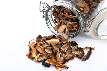 Close-up of dried homemade mushrooms poured out of a vintage glass jar on a white background.