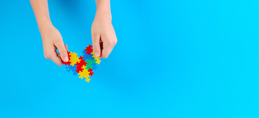 Fototapeta premium Child hand holding colorful heart on light blue background. World autism awareness day concept