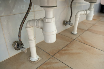 Close up of white plastic pipe drain under washing sink in bathroom.