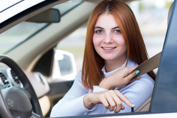 Wide angle view of young redhead woman driver fastened by seatbelt driving a car smiling happily.