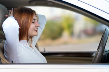 Young redhead woman driver fastened by seatbelt resting in a car smiling happily.