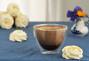 Glass cup with coffee with milk on the table, next to homemade marshmallows. Spring flowers in a vase next to zephyr. Horizontal orientation. Selective focus a cup of coffee.