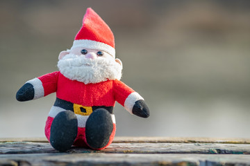 Close up of small santa clause toy on wooden bench outdoors.