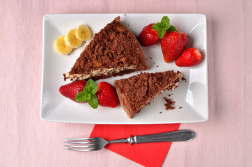 Mole hole cake - homemade cake with whipped cream, banana, strawberries and fresh mint leaves on white decorative shaped plate. Pink place setting. Top view.