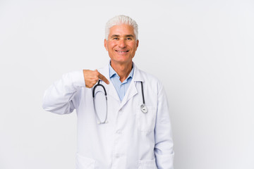 Mature caucasian doctor man person pointing by hand to a shirt copy space, proud and confident