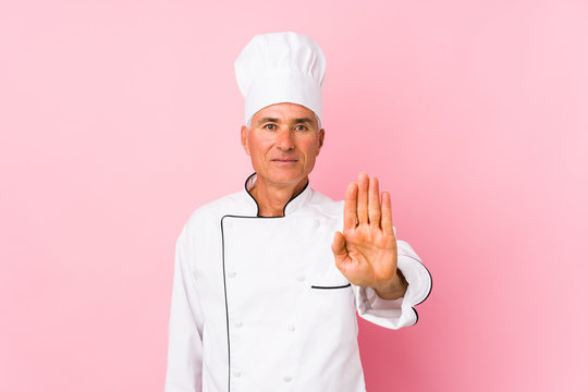Middle aged cook man isolated standing with outstretched hand showing stop sign, preventing you.