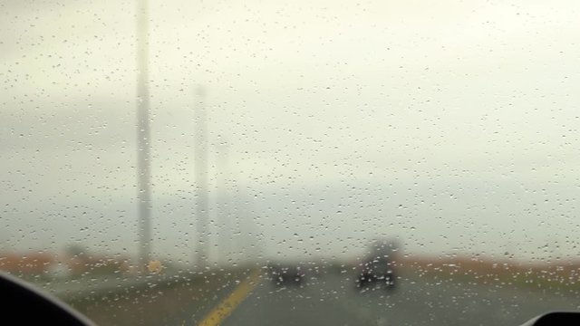 defocused of rain drops on windshield and Driving on rainy highway. Rain drops water on car window background. Blured background with rains drop on glass and car light