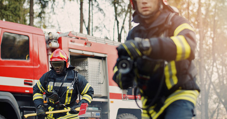 Two firefighters in fire fighting operation, fireman in protective clothing and helmet with...