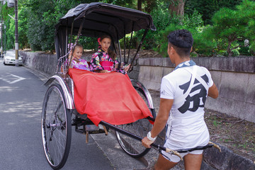 KYOTO, JAPAN 08.2019 Japanese rickshaw rides kimano-dressed girls. - obrazy, fototapety, plakaty