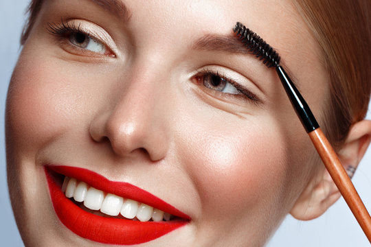 Beautiful girl with red lips and classic makeup with cosmetic brow brush in hand. Beauty face.