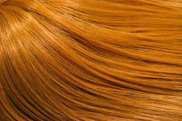 A closeup view of a section of glossy straight ginger hair in a wavy style. Shiny highlight abstract background texture, synthetic extensions. Beauty salon. Hair care, healthy.