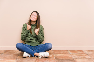 Young caucasian woman sitting on the floor isolated raising both thumbs up, smiling and confident.