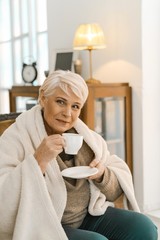 Cheerful Senior Woman Wrapped In A Warm Knitted Plaid Relaxing At Home