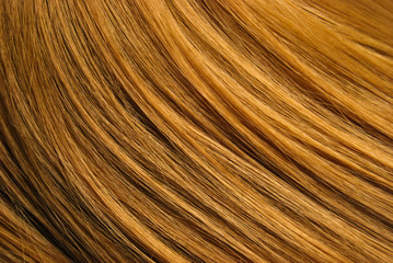 A closeup view of a section of glossy straight ginger hair in a wavy style. Shiny highlight abstract background texture, synthetic extensions. Beauty salon. Hair care, healthy.