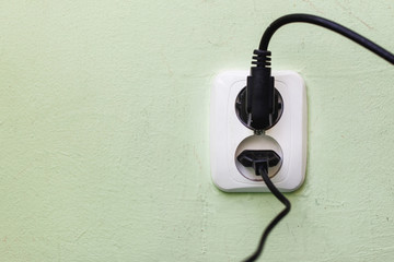 Grunge white electrical socket. Black cable plugged into electricity.