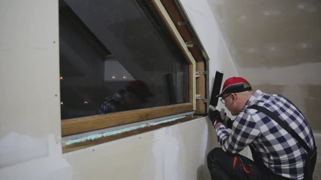 Handyman, construction man installing PVC window in a new insulated and filled dry wall attic.
