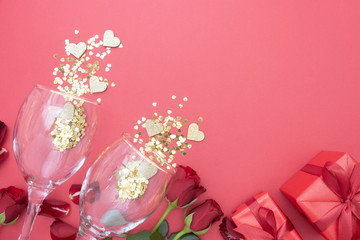 Valentine's day background, birthday or party abstract flat lay. Two empty glasses for champagn, gift boxes and red roses flowerse on pink background with golden glitter. Copy space.