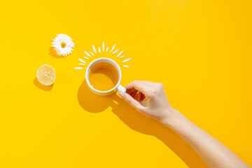 Hot drink, cup of tea with chamomile and lemon on a yellow background