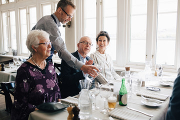Owner serving water to senior people sitting at restaurant
