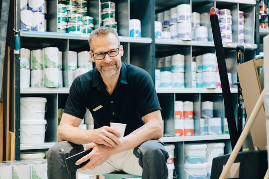 Portrait Of Smiling Salesman Sitting On Stool In Store