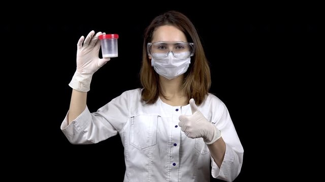 Young woman doctor checks sperm tests. A woman examines a test jar, then shows a thumb up. Positive semen analysis. On a black background.
