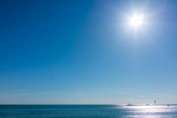 Obraz premium Clear sky and bright sun over the sea with a breakwater and a lighthouse