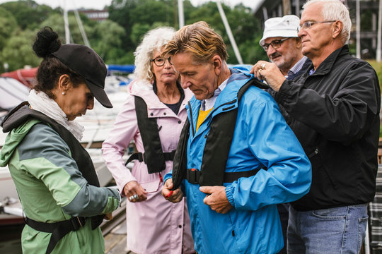Senior man helping friend in wearing life jacket during boat master course