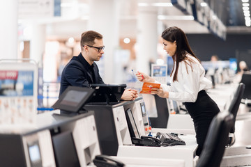 Business trip. Handsome young businessman in suit holding his passport and talking to woman at airline check in counter in the airport