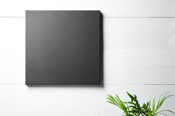 A black cotton canvas and leaves of green plant  on white wooden background. Stretched clean canvas...