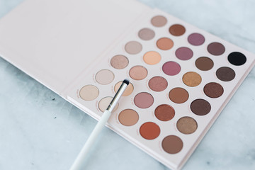 Neutral eyeshadow palette with brushes on marble background
