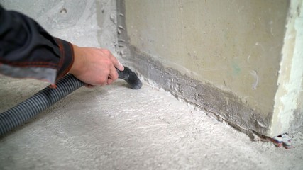 vacuum cleaner construction on the background of concrete walls and floors. A worker removes dust with a vacuum cleaner from a concrete floor.