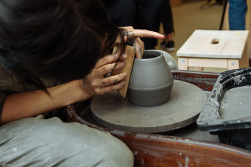 The girl sits at the Potter's wheel and creates a pot of ceramics. A Potter makes pottery out of clay behind a mechanical circle