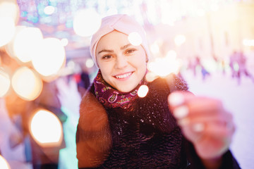 Portrait young beautiful girl smiling and holding sparkler, evening illumination background