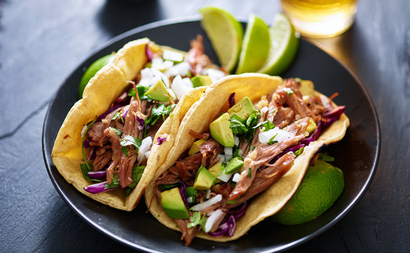 plate of mexican carnita tacos with beer in background