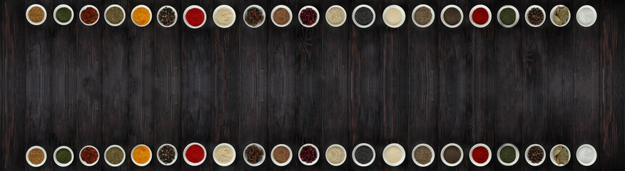 A wide selection of spices in a row on a dark background, with empty space for text or label.