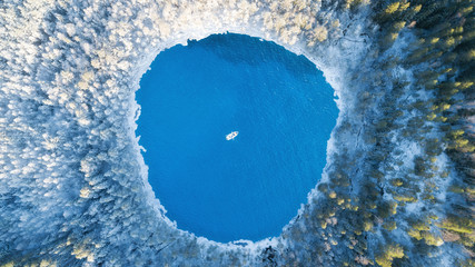 Aerial view of the winter lake with clear blue sea water and boat. Abstract picture. Above captured with a drone. Beautiful snowy forest.