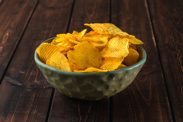 close-up view on green plate of delicious corrugated golden potato chips fried and salted on a brown wooden background, concept of fast food