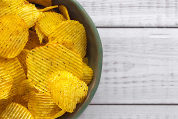 close-up view on green plate of delicious corrugated golden potato chips fried and salted on a bright white wooden background with copy space, top view